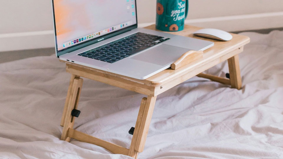Laptop egy fa laptopállványon az ágyon, kényelmes otthoni használathoz és a jobb szellőzés érdekében.
